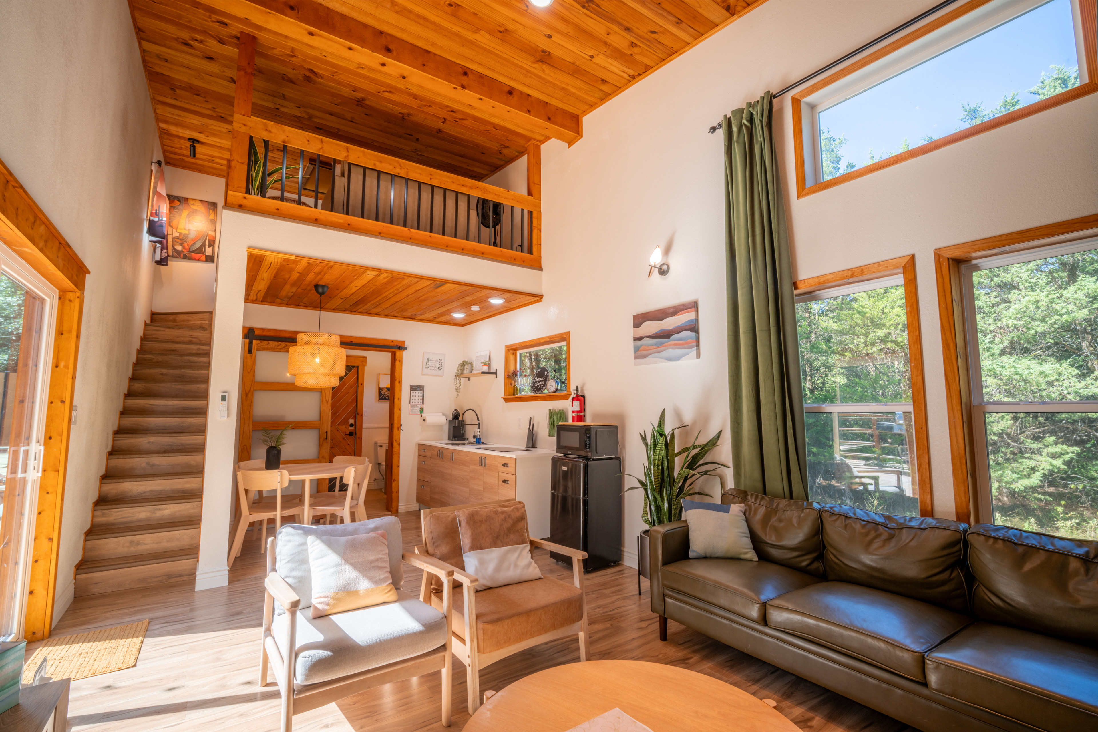 NestScape living area with a timber loft, kitchen, and tall woodland-facing windows